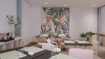 Un'area ristorazione moderna con tavoli, sedie e un grande murale tropicale sulla parete.