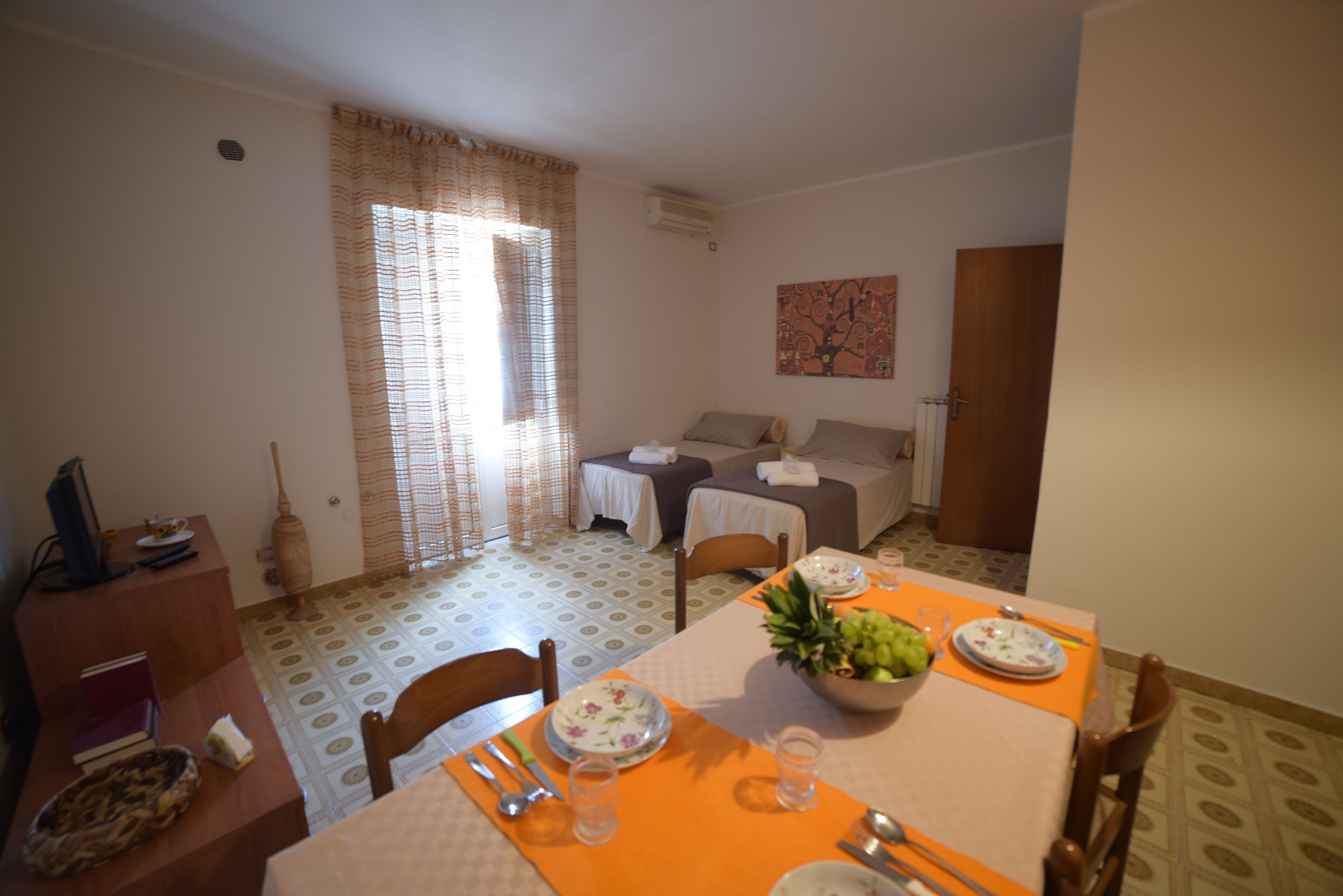 A dining area with a table set for two, a sofa, and a small table with a vase.