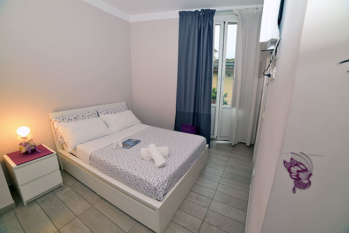 A neatly made bed with a floral bedspread, a bedside lamp, and a small table with a purple object on it.