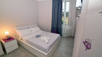 A neatly made bed with a floral bedspread, a bedside lamp, and a small table with a purple object on it.