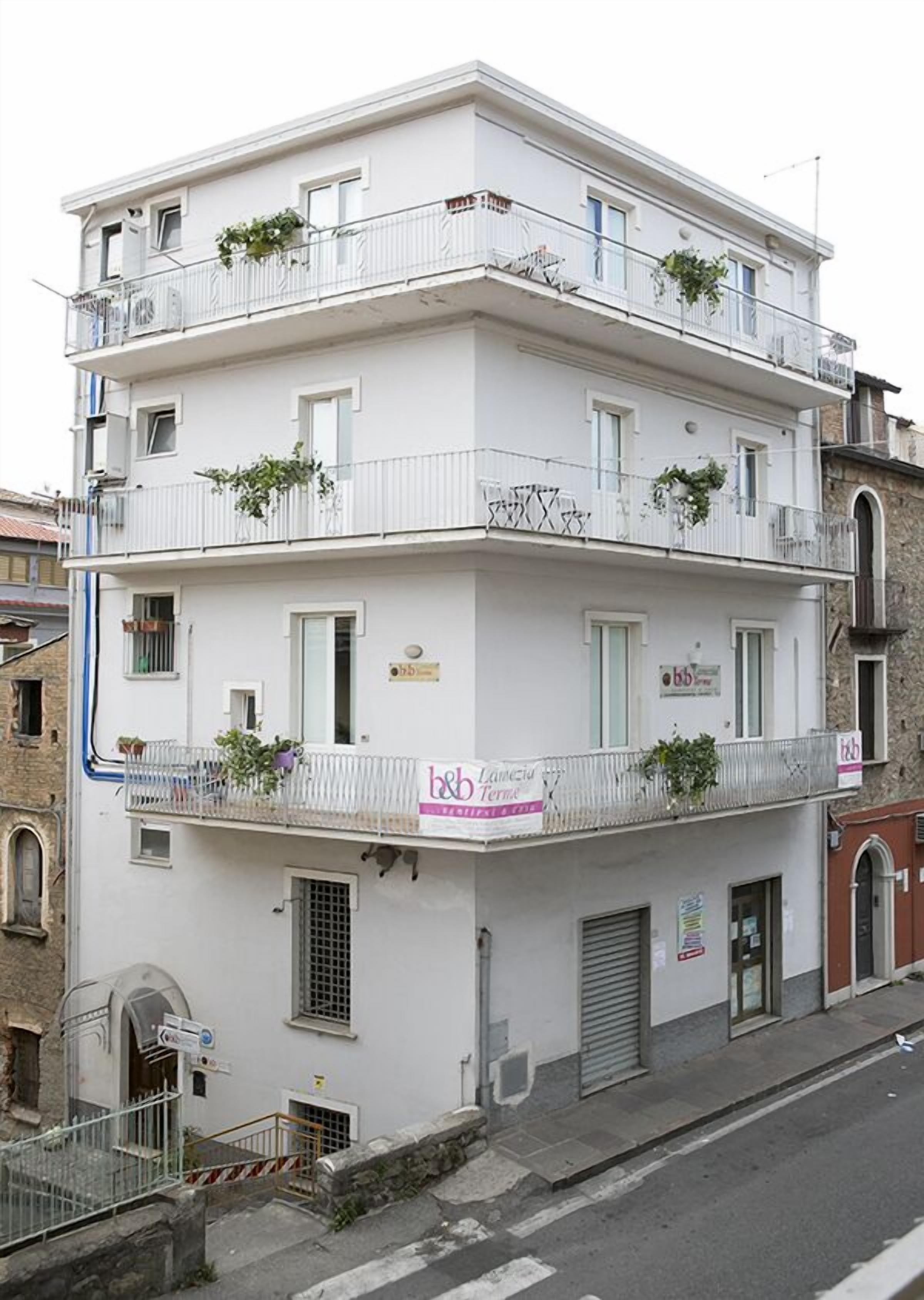 A multi-story building with balconies, some with plants. There is a sign for 'b&b Lamezia Terme' on the ground floor.