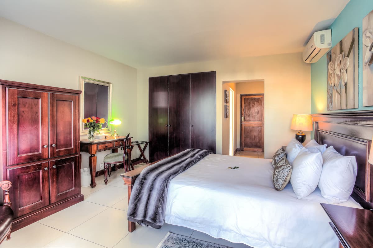 A hotel room with a large bed, wooden wardrobe, desk with chair, and a desk lamp.