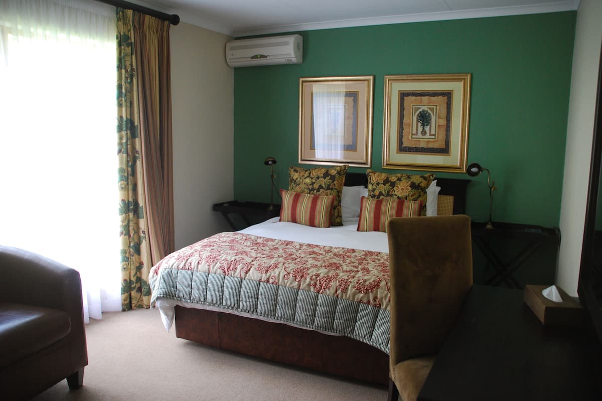 A hotel room with a bed, a chair, a desk, and two framed pictures on the wall.