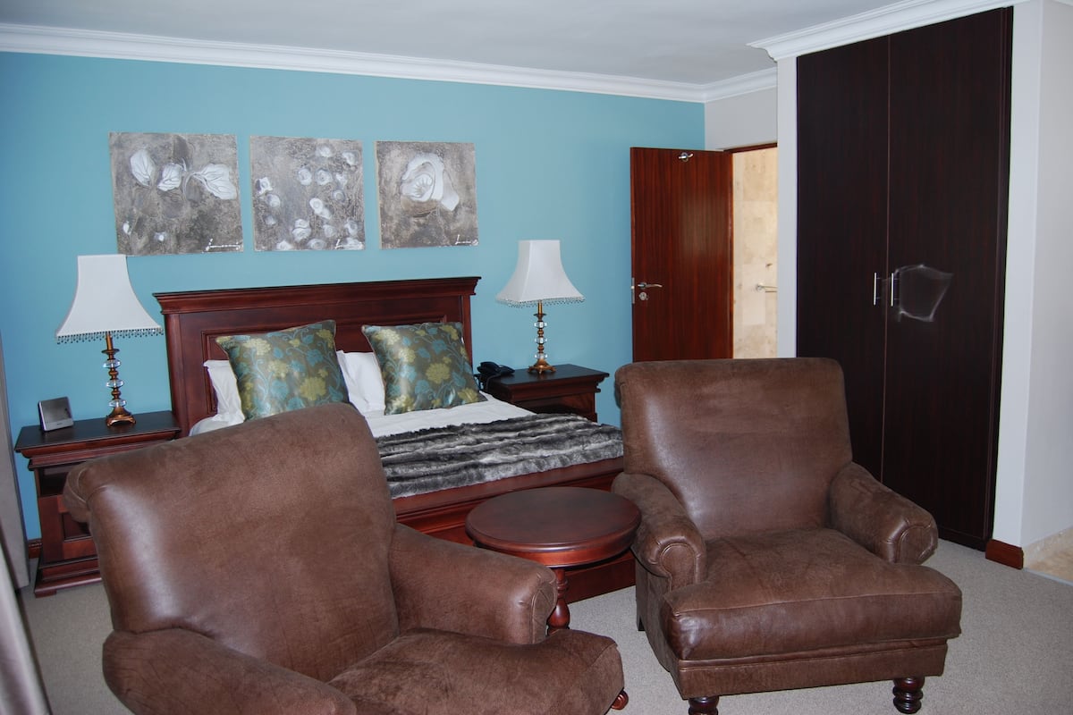 A bedroom with a bed, two armchairs, a nightstand, and a wardrobe.