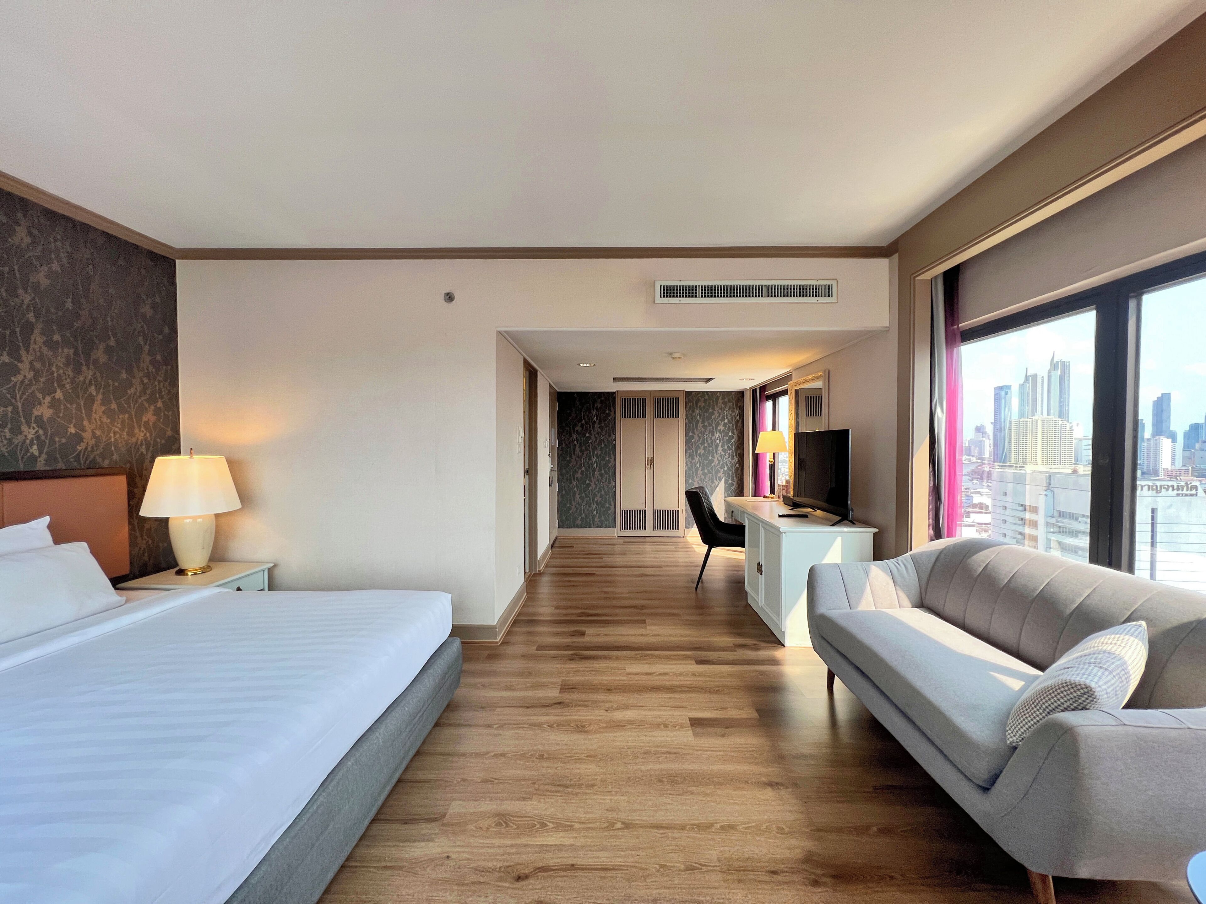 Habitación de hotel con cama, escritorio, sofá y un amplio ventanal con vistas a la ciudad.