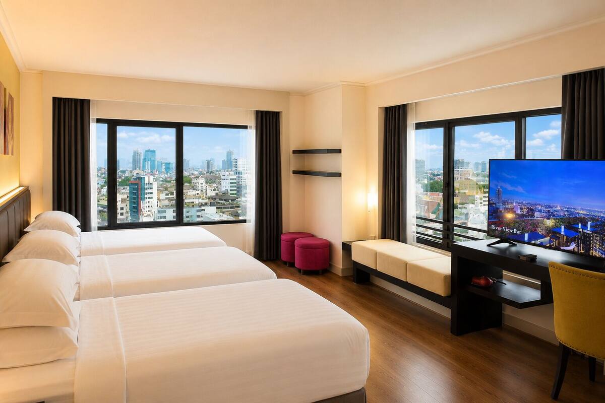 Une chambre d’hôtel avec deux lits, un bureau, une télévision et de grandes fenêtres donnant sur la ville.