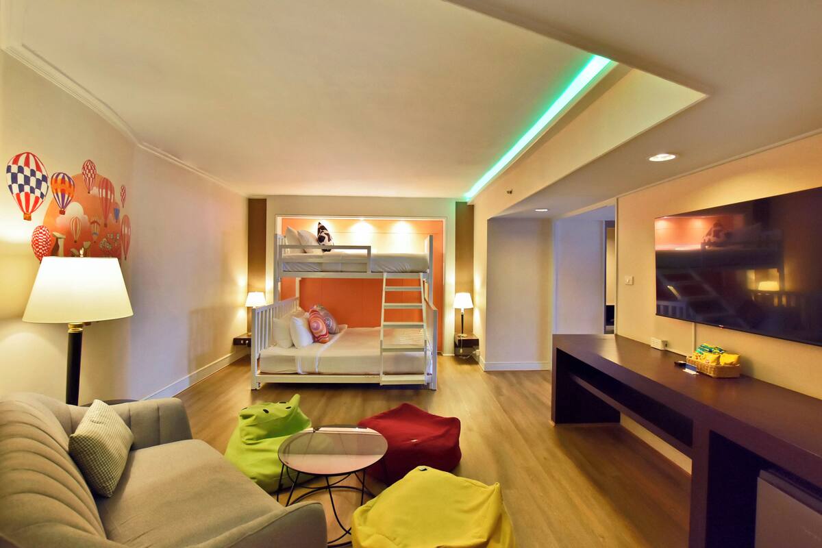 Une chambre d’hôtel moderne équipée d’un lit superposé, d’un canapé, d’une petite table et d’un téléviseur.