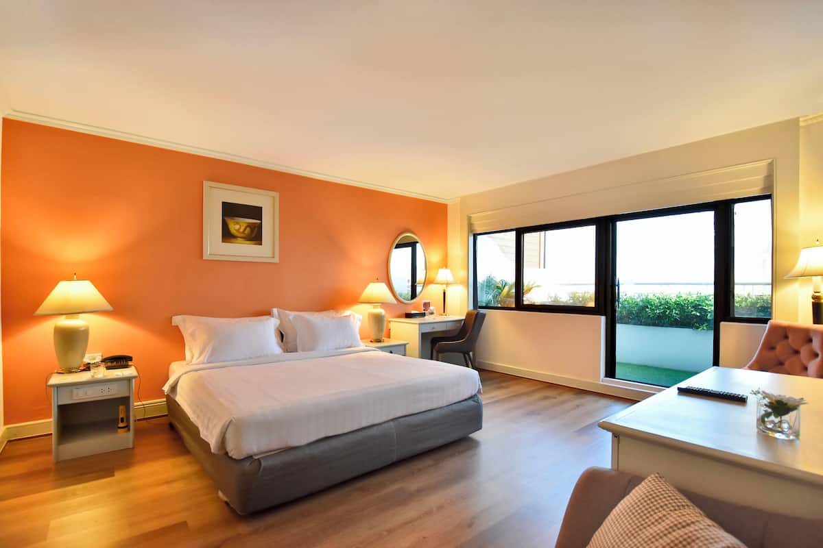 Une chambre d’hôtel avec un lit, des tables de chevet, un bureau, une chaise et une grande fenêtre.