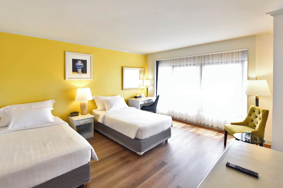 Une chambre d’hôtel avec deux lits, un bureau, une chaise et une grande fenêtre avec des rideaux.