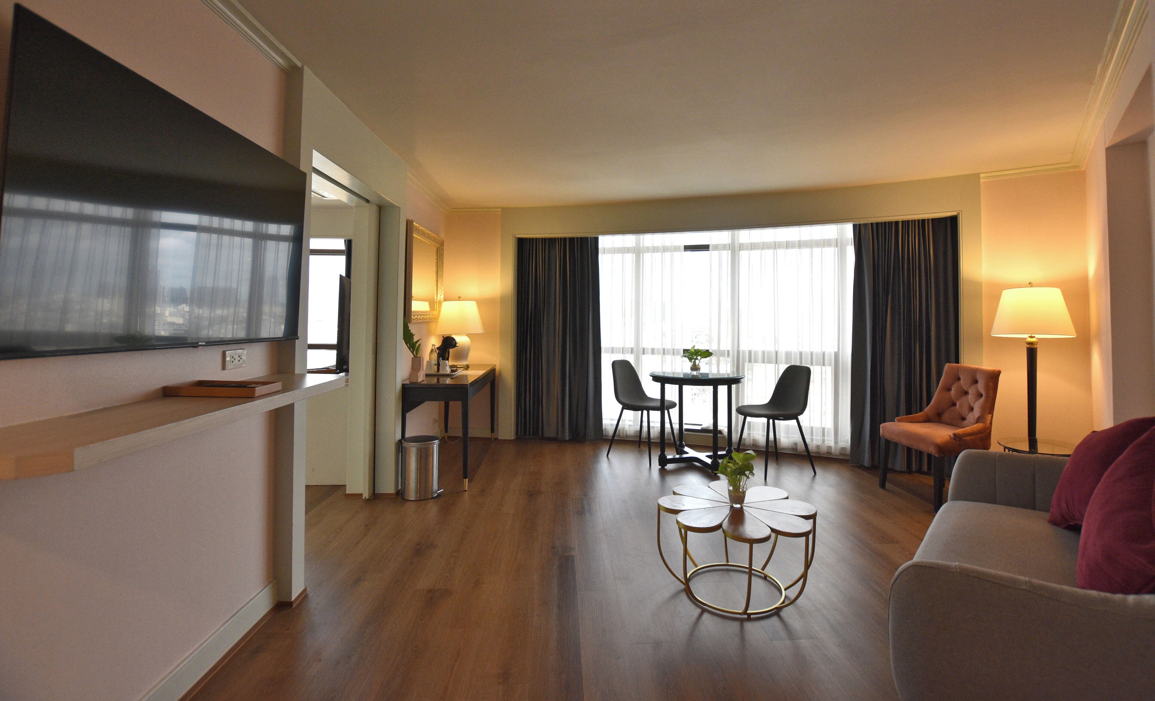 Ein Hotelzimmer mit Fernseher, einer Essecke mit Tisch und Stühlen, einer Couch und einer Lampe.