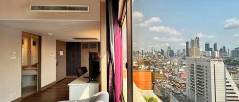 A modern hotel room with a city view, a desk, a chair, and a large window.