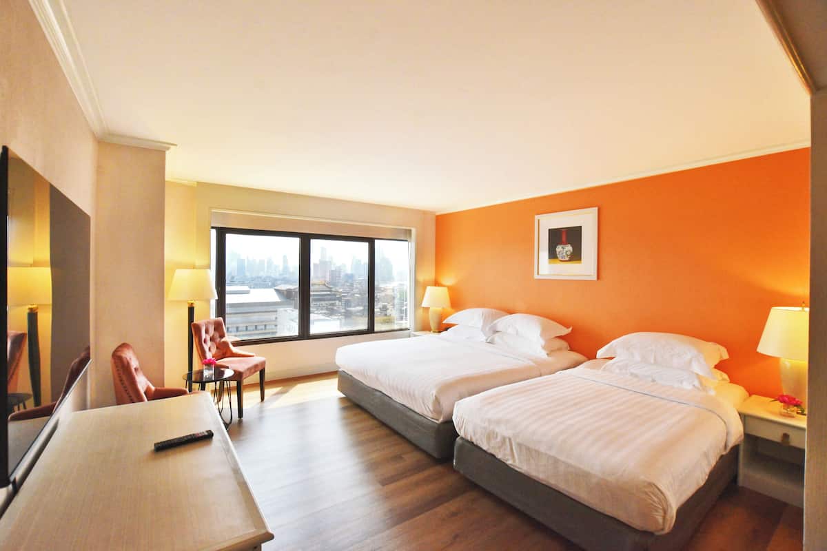Une chambre d’hôtel avec deux lits, un bureau, une chaise et une grande fenêtre donnant sur la ville.