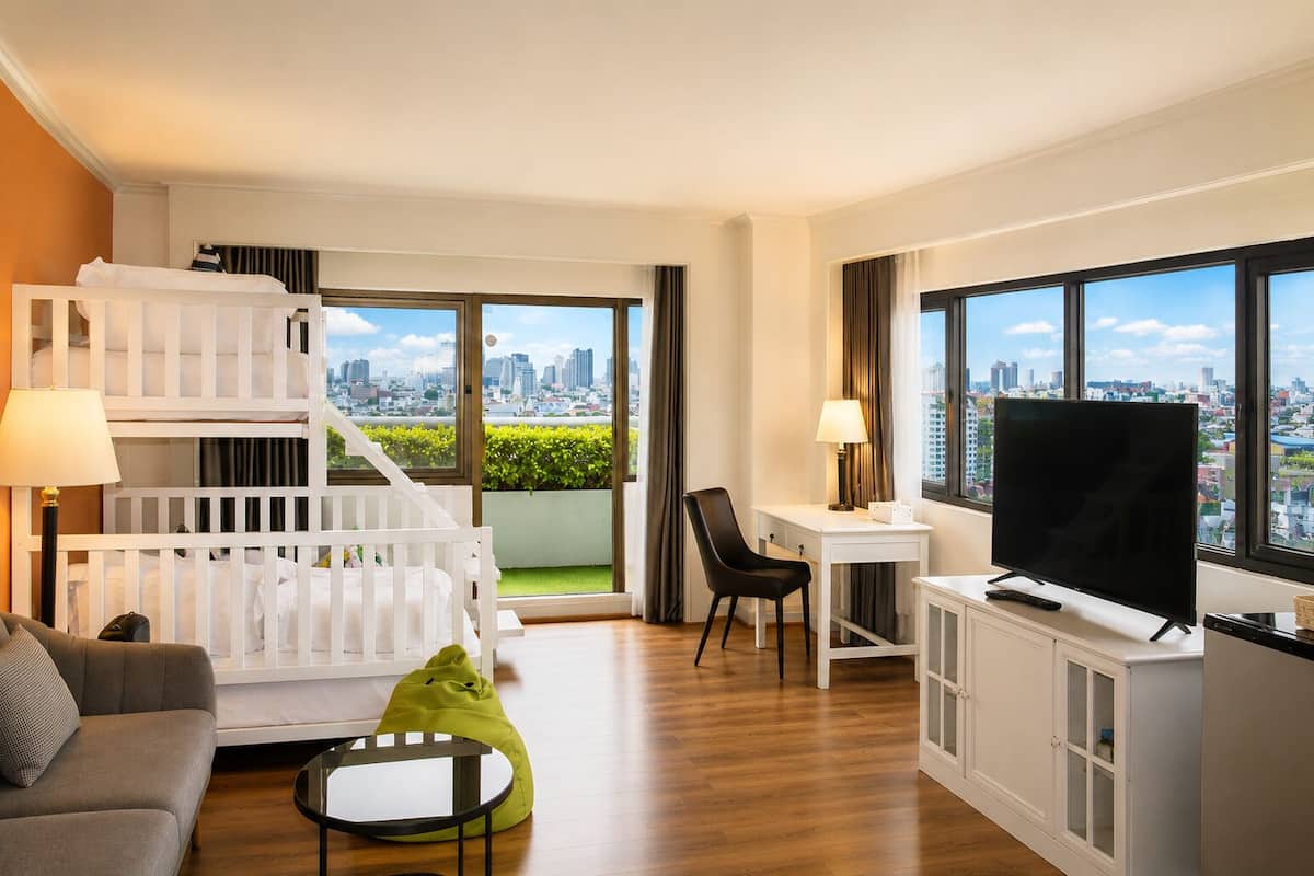 Une chambre d’hôtel moderne avec vue sur la ville, un bureau blanc, un téléviseur à écran plat, un canapé et un lit superposé.