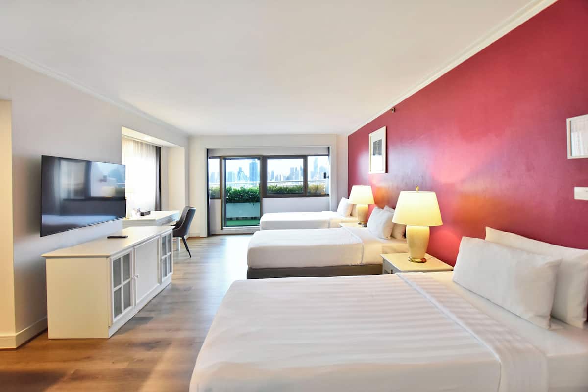 Une chambre d’hôtel avec deux lits, une télévision, un bureau et une grande fenêtre donnant sur la ville.