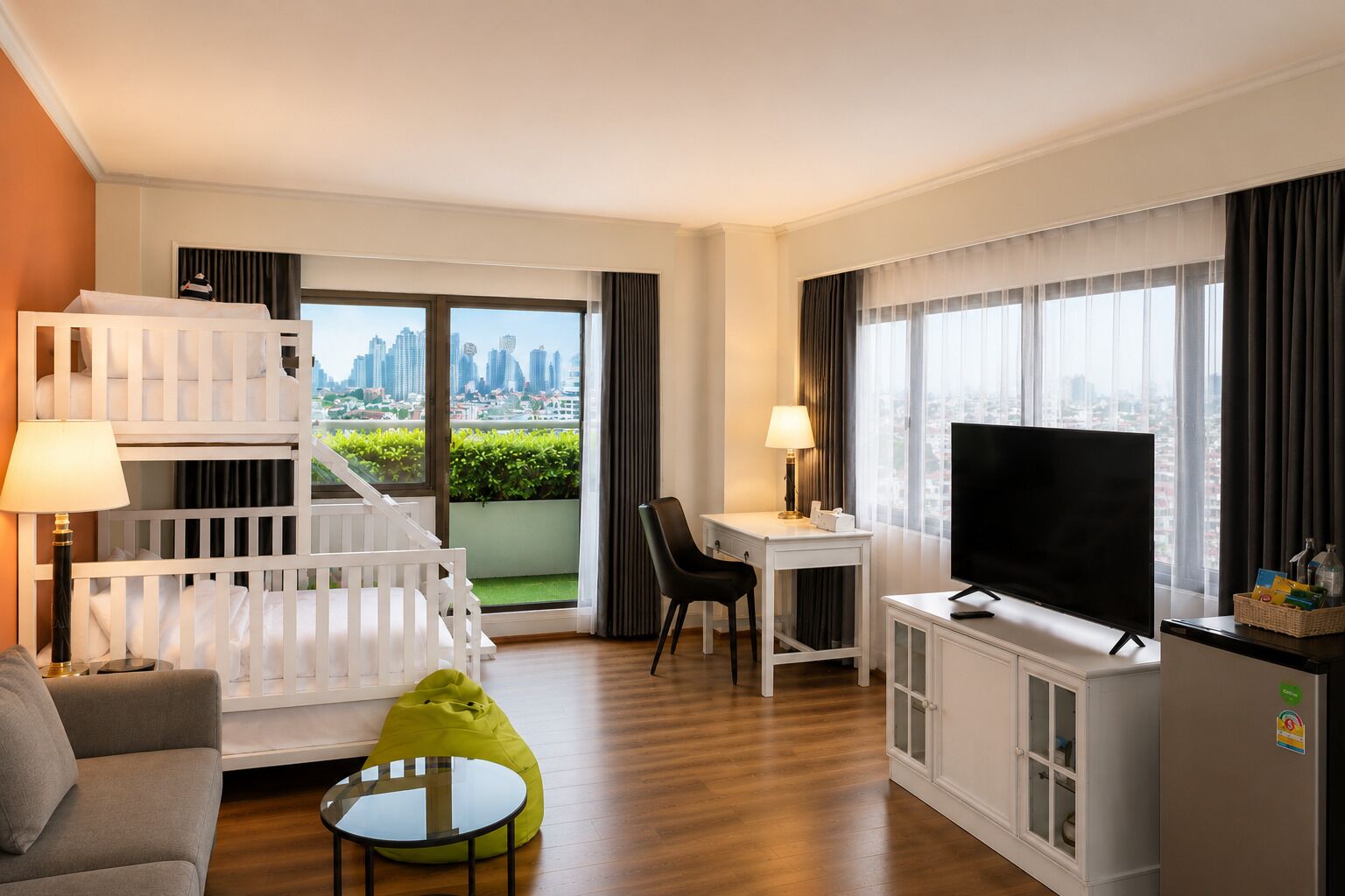 A hotel room with a balcony, a TV, a desk, a chair, a sofa, and a small table.