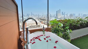Un balcón con una bañera llena de pétalos de rosa, vistas al horizonte de la ciudad y abundante follaje.