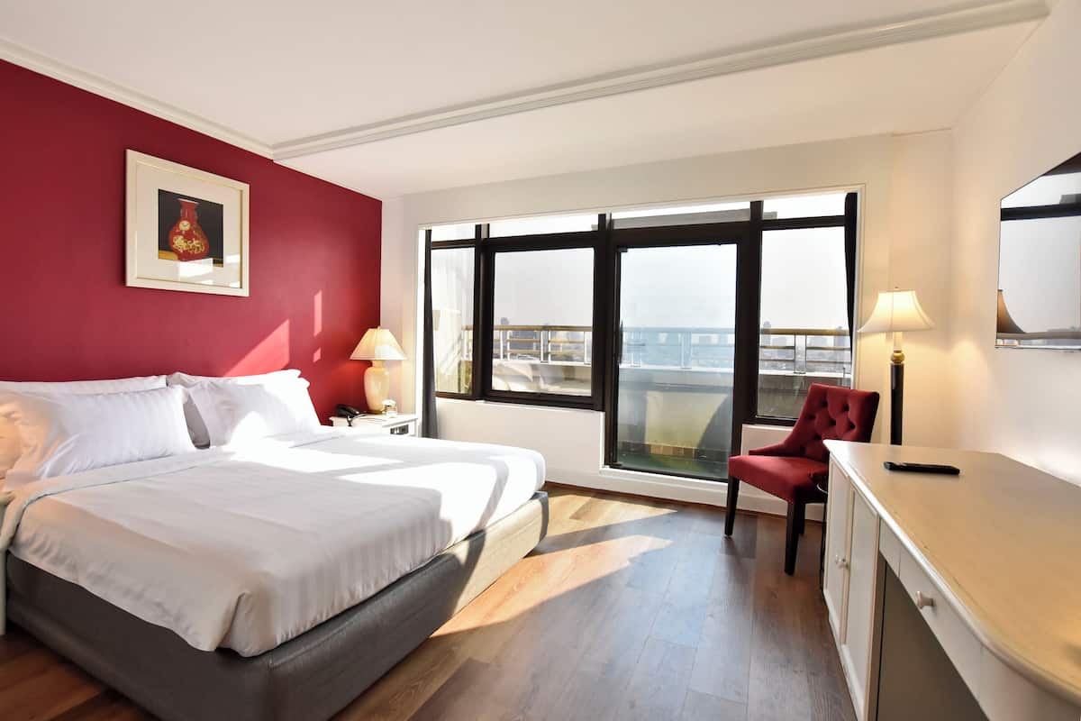 Une chambre d’hôtel avec un lit, un bureau, une chaise, une fenêtre donnant sur un paysage agréable et une lampe.