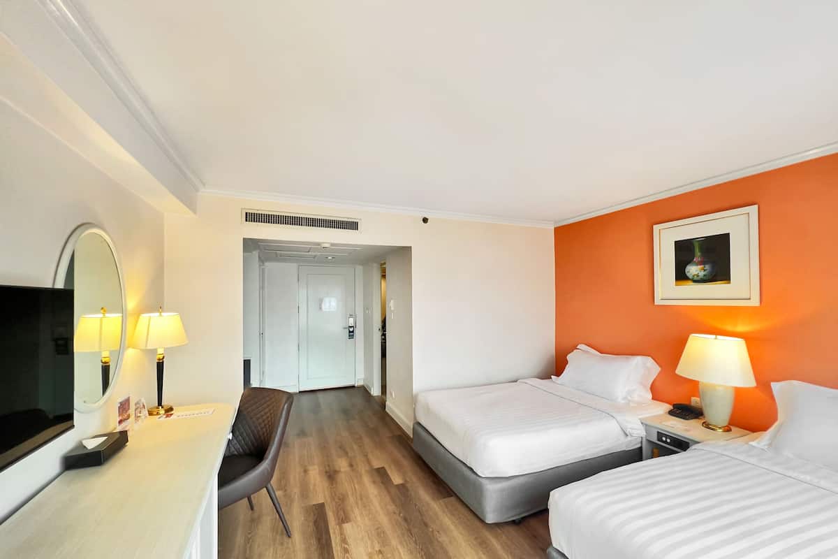 Une chambre d’hôtel avec deux lits, un bureau avec une chaise, une télévision et un tableau au mur.
