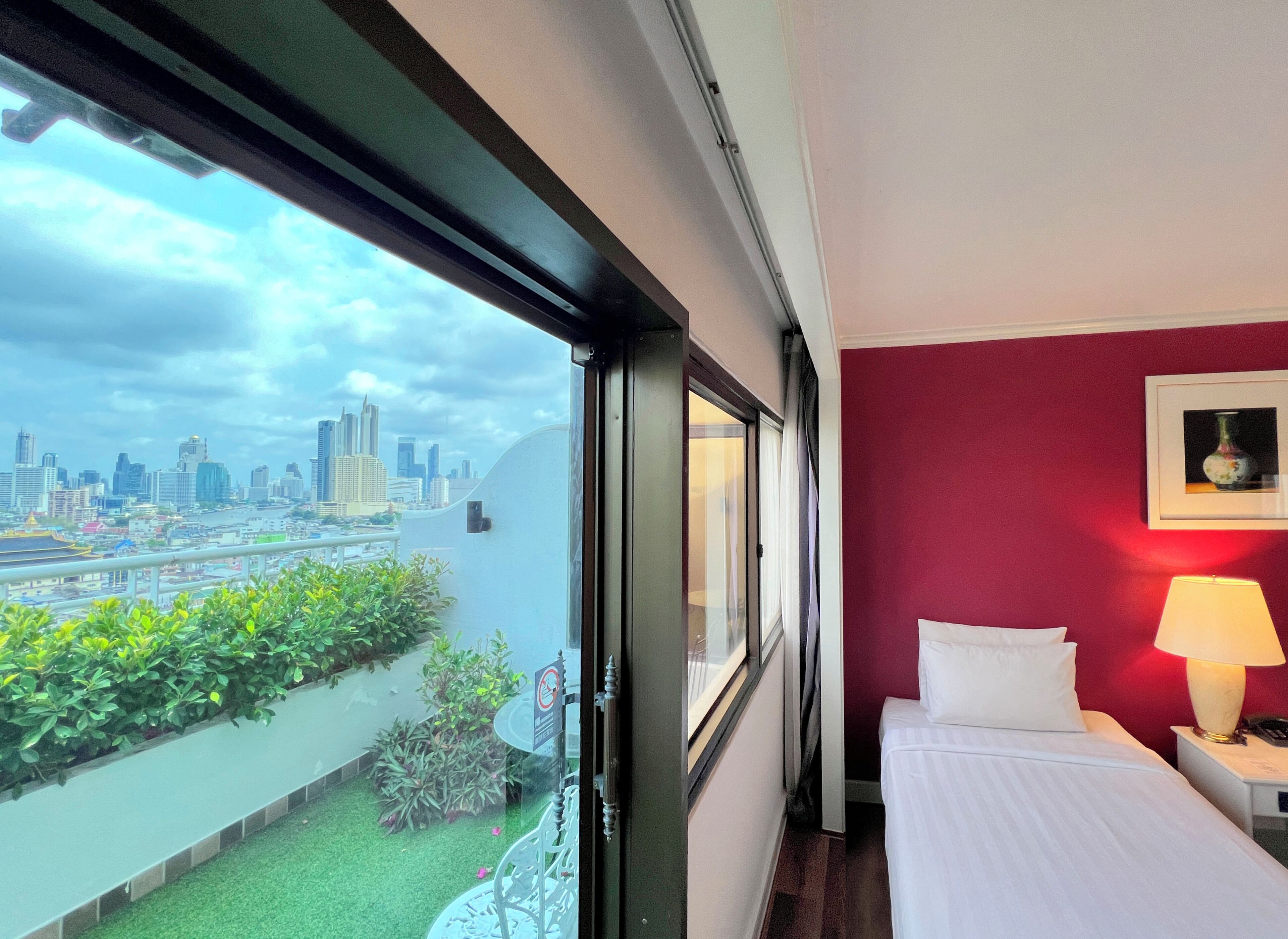 A hotel room with a city view, a bed, a nightstand, a lamp, and a window.