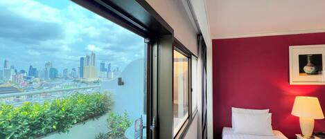 Habitación de hotel con vista a la ciudad, una cama, una mesita de noche, una lámpara y una ventana.