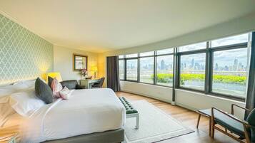 Habitación de hotel con cama, escritorio, silla y ventanas amplias que dan a una vista de la ciudad.