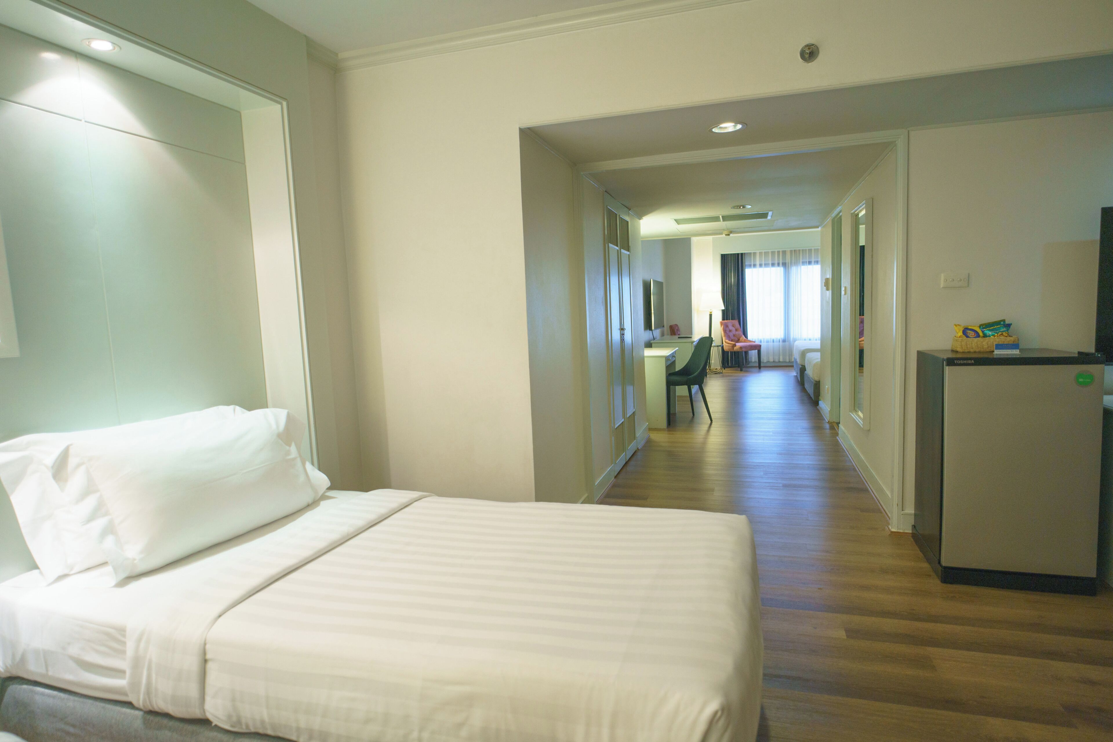 A hotel room with a bed, a desk, a chair, and a refrigerator.