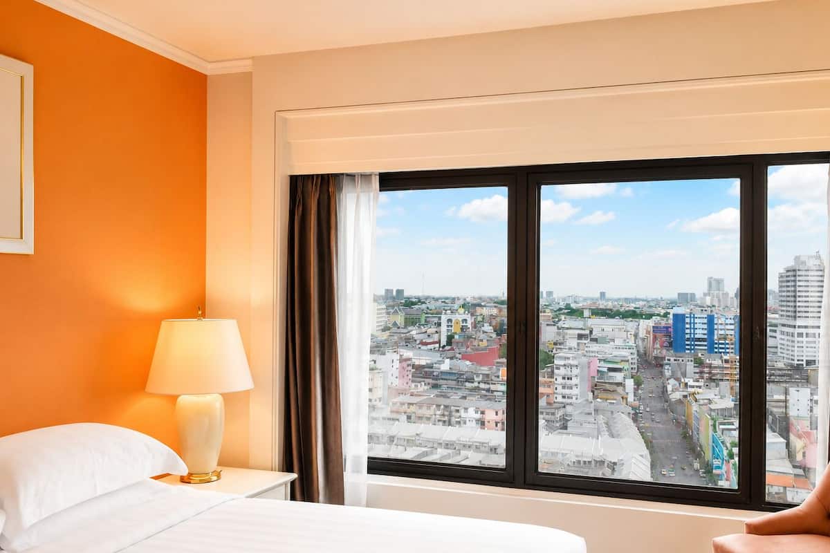 Une chambre d’hôtel avec une grande fenêtre, un lit, une table de chevet et une lampe.