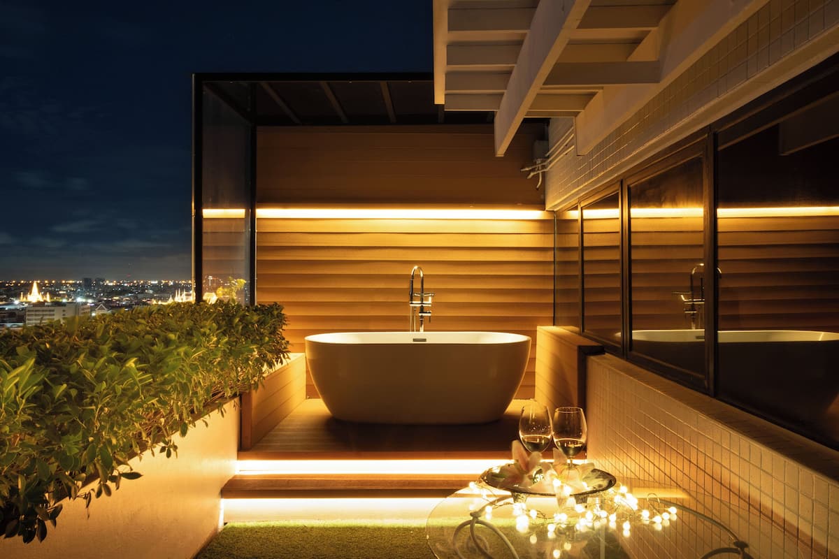 Une salle de bain moderne avec une baignoire sur pieds, une table en verre avec un verre à vin, et une vue sur la ville la nuit.