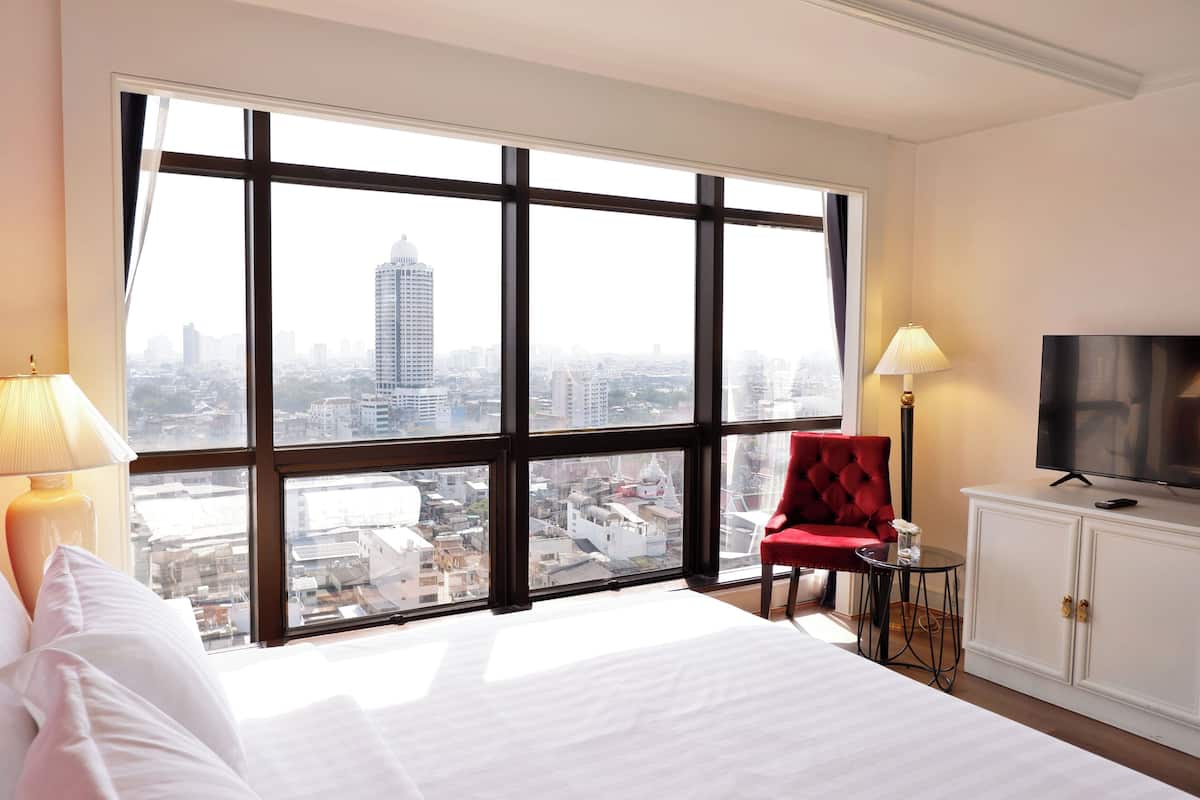 Une chambre d’hôtel avec une grande fenêtre, un lit, un fauteuil rouge, une télévision et une petite table.