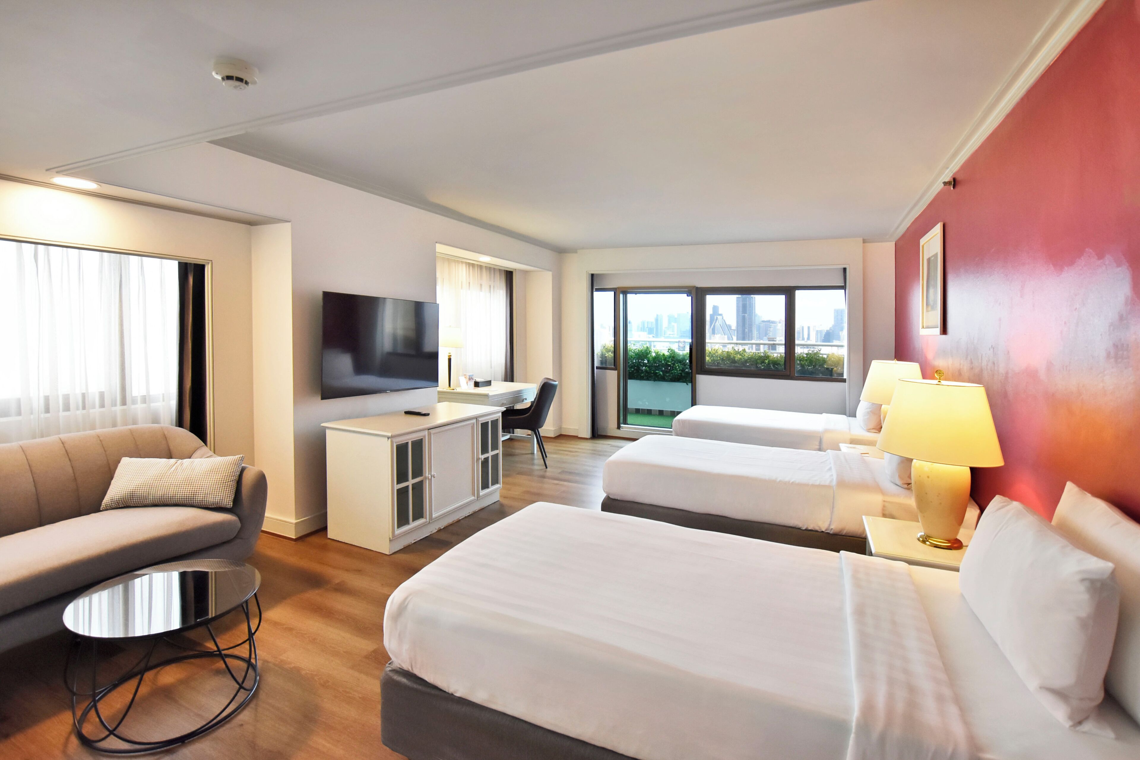 A hotel room with two beds, a sofa, a TV, a desk, and a large window with a city view.
