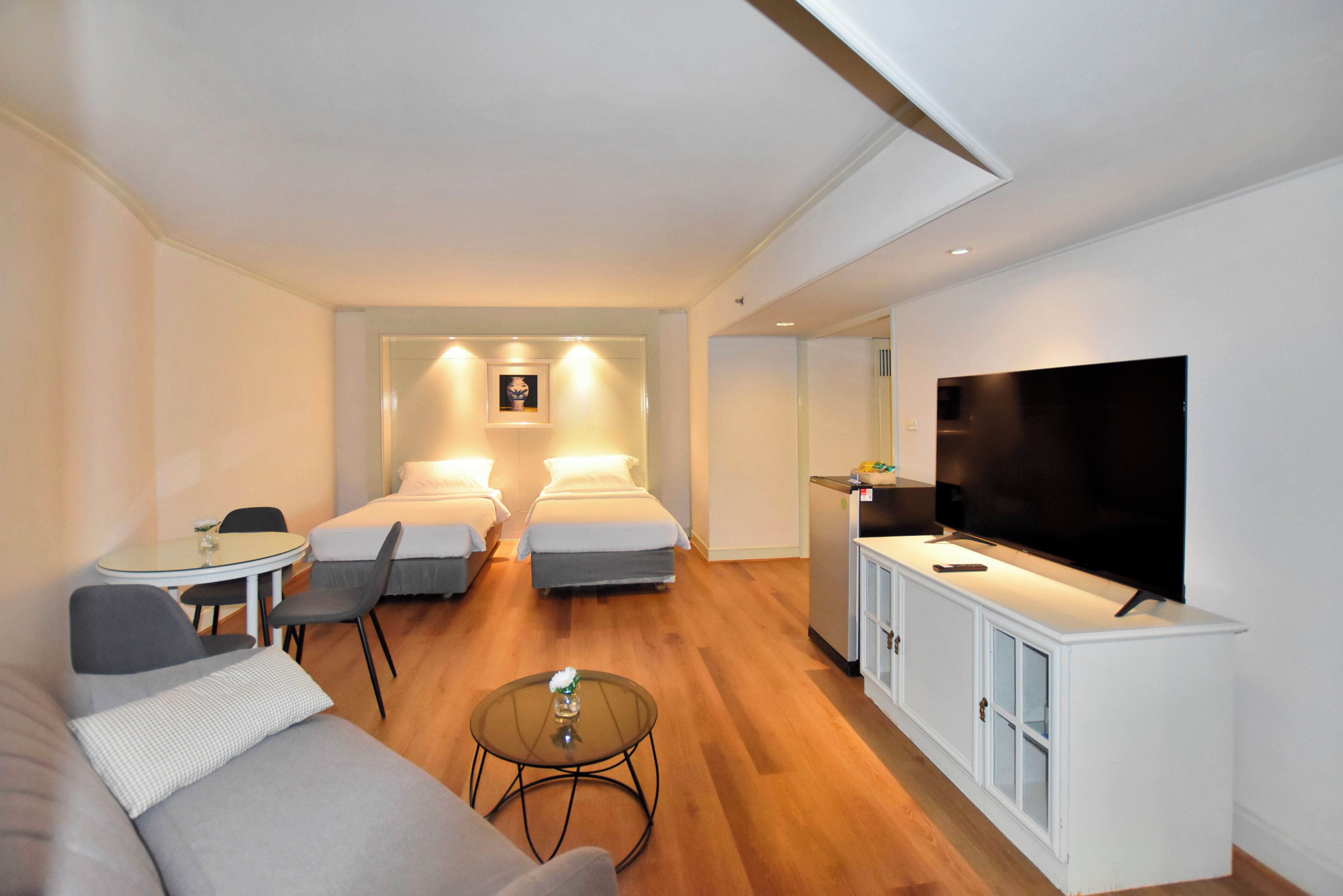 A hotel room with a sofa, two single beds, a TV, a small table, and a cabinet.