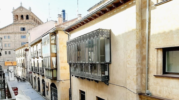 A narrow street with buildings featuring balconies and large windows. - Hosteria Sara by gaiarooms (Salamanca)