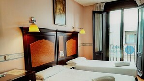 A hotel room with two single beds, a wooden headboard, a desk with a lamp, and a window with a view of the city. - Hosteria Sara by gaiarooms (Salamanca)