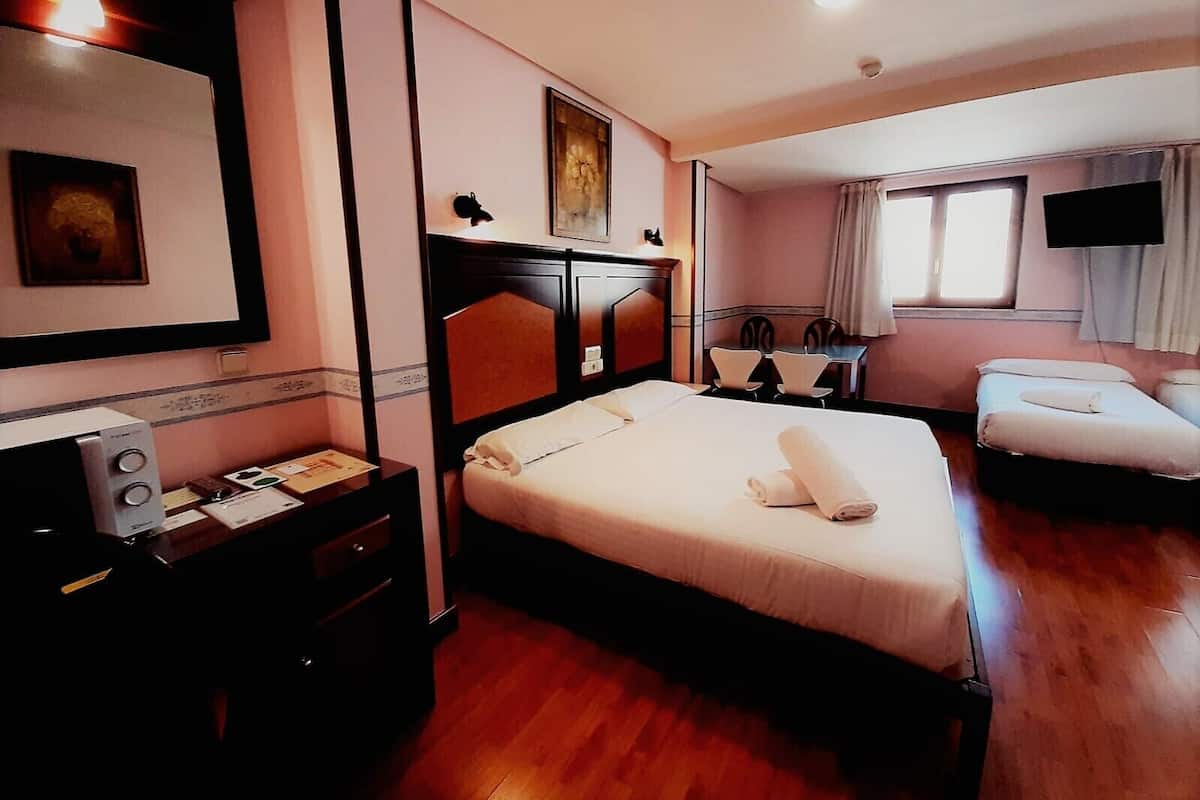 A hotel room with a large bed, a desk with a telephone, a chair, a small table, and a television.