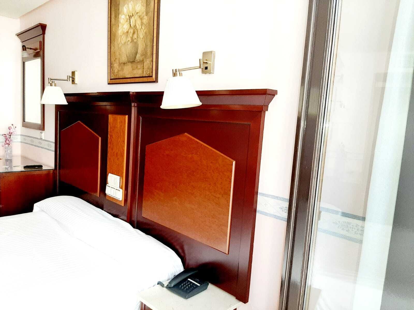 Una habitación de hotel con una cama grande, una mesita de noche con un teléfono, un espejo y un cuadro en la pared.