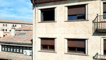Un immeuble à plusieurs étages, doté d’une façade en pierre, de nombreuses fenêtres avec volets et d’un balcon situé sur le côté droit.