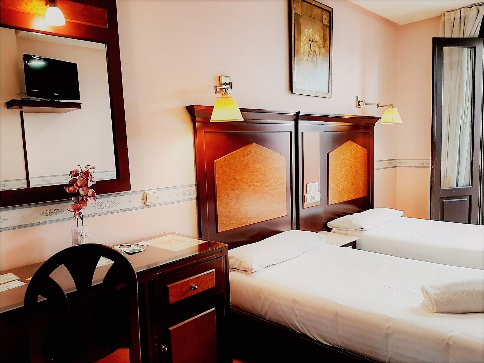 Habitación de hotel con dos camas, un escritorio, una silla, un televisor y un cuadro en la pared.