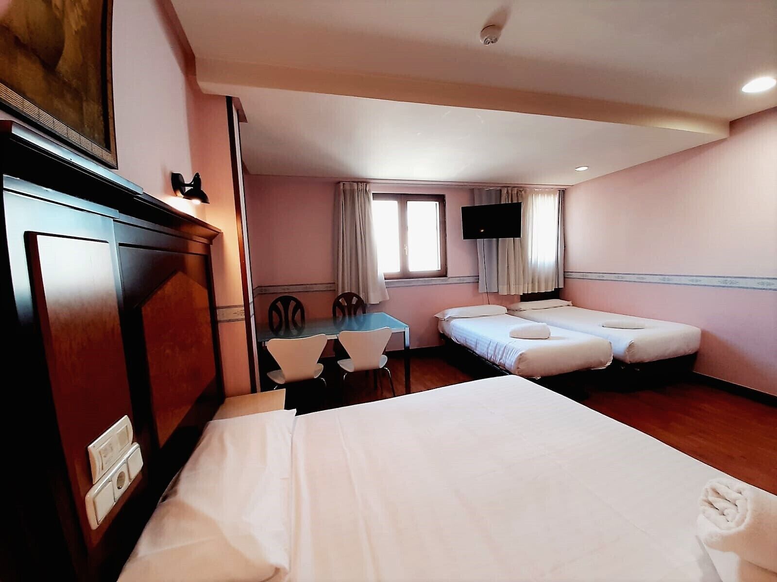 Habitación de hotel con dos camas, un escritorio con sillas, un televisor y una ventana con cortinas.
