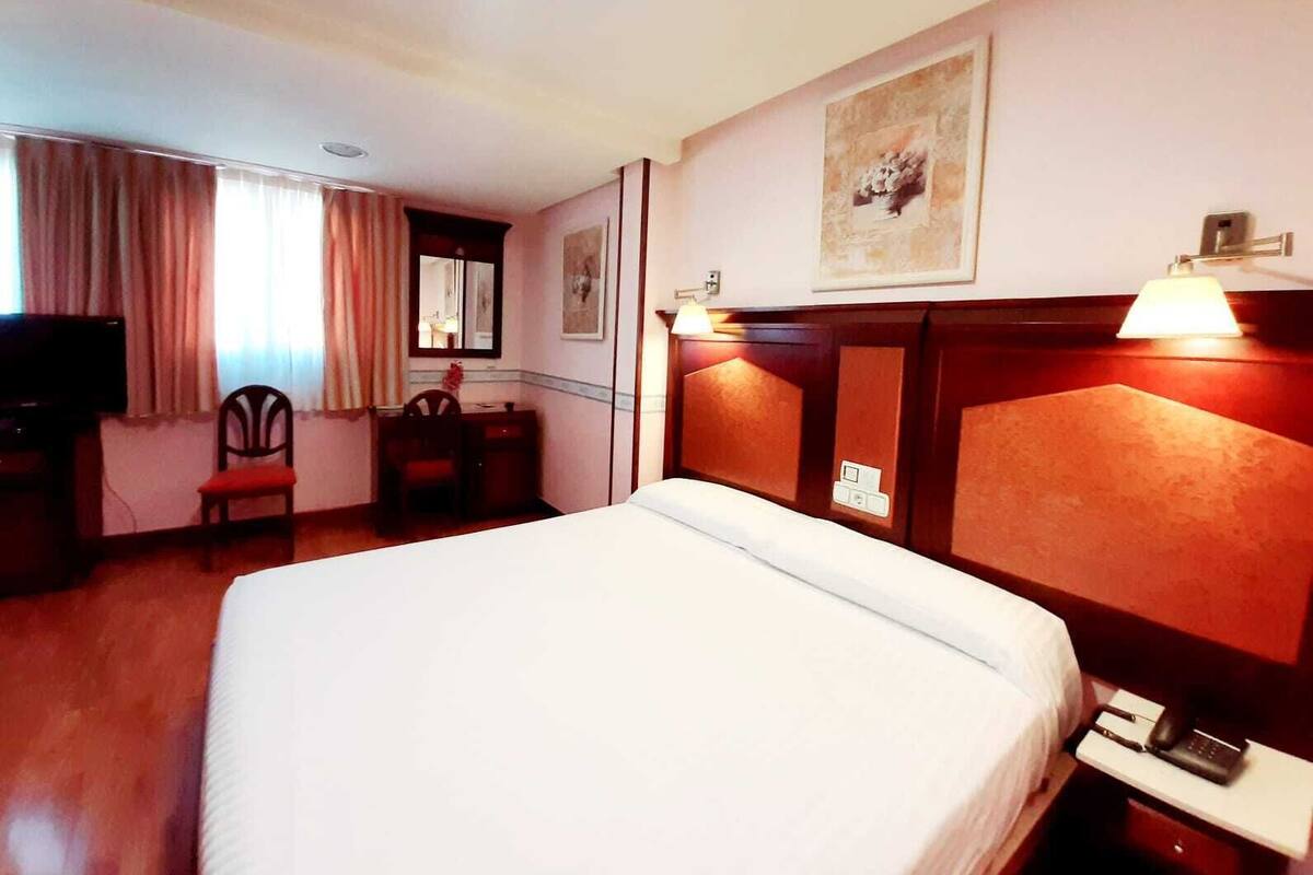 A hotel room with a large bed, a desk with a chair, a television, and a painting on the wall.