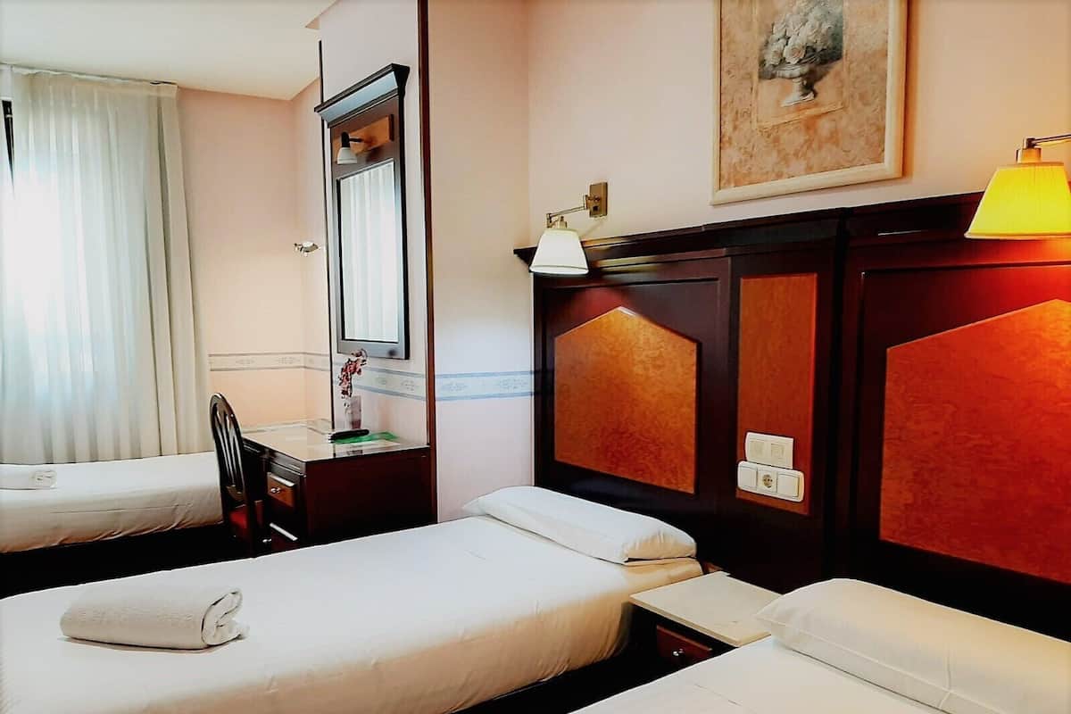 A hotel room with two single beds, a desk with a chair, a mirror, and a painting on the wall.