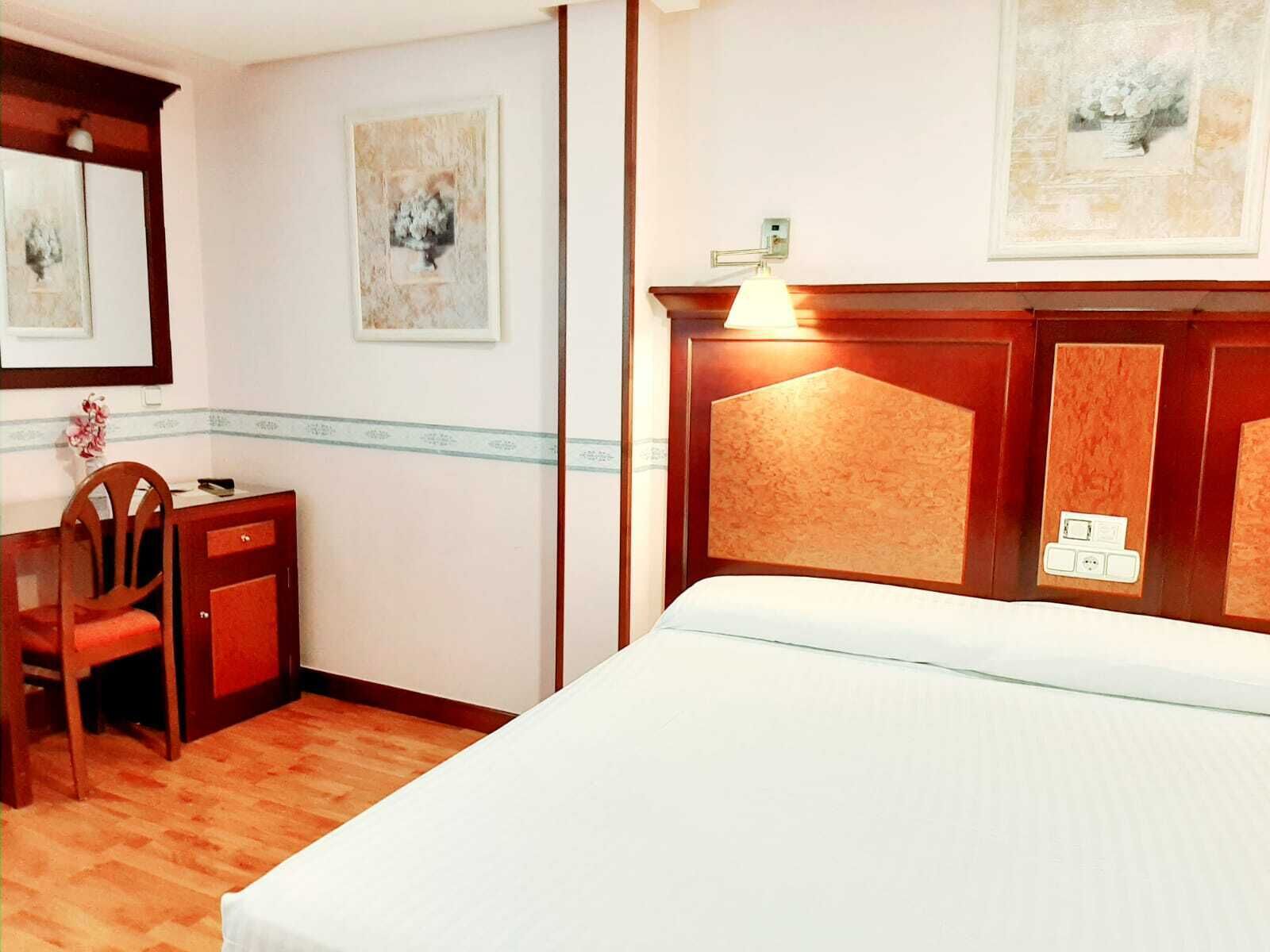 A hotel room with a bed, a desk with a chair, and two framed pictures on the wall.