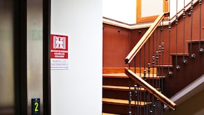 A staircase with wooden steps and metal railings, a door with a number 2 sign, and a safety sign on the wall. - Hosteria Sara by gaiarooms (Salamanca)