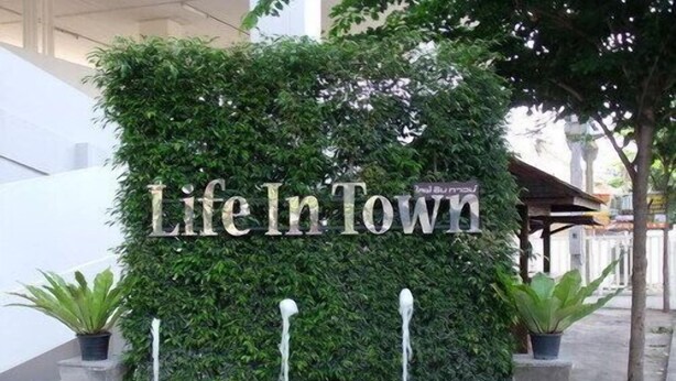 A sign reading "Life In Town" with a lush green hedge backdrop and potted plants at the base. - Life In Town Chiangmai (Chiang Mai)
