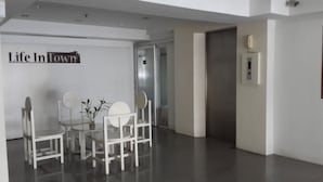 A modern interior with a dining area featuring a glass table and white chairs, a sign reading "Life In Town", and a door leading to another room. - Life In Town Chiangmai (Chiang Mai)