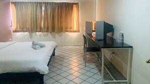 A hotel room with a bed, a desk with a computer, a chair, and a window with curtains. - Life In Town Chiangmai (Chiang Mai)