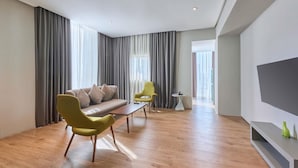 A modern living room with a sofa, two chairs, a coffee table, and a TV. - ibis Styles Dubai Jumeira (Dubai)