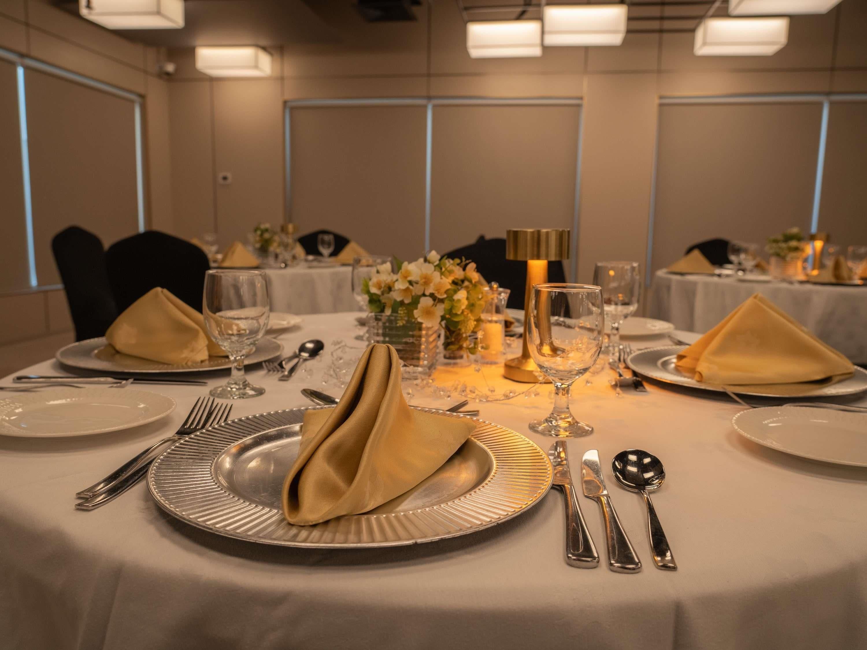 A dining table set with plates, cutlery, and napkins, with a vase of flowers and a candle centerpiece.
