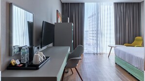 A hotel room with a bed, a desk with a TV, a chair, a small table, and a window with curtains. - ibis Styles Dubai Jumeira (Dubai)
