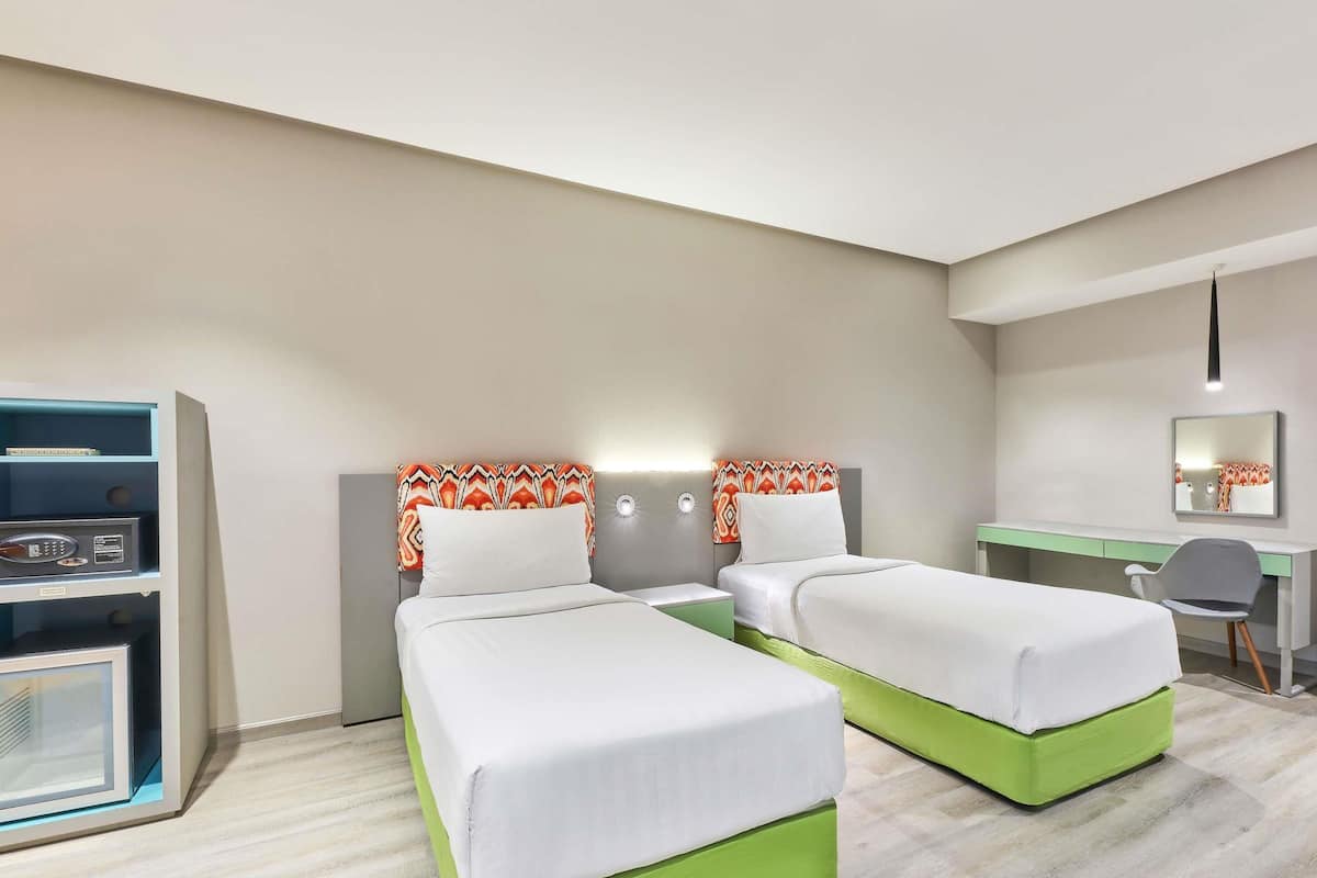 Una habitación de hotel con dos camas individuales, un escritorio, una silla, un minibar y un espejo.