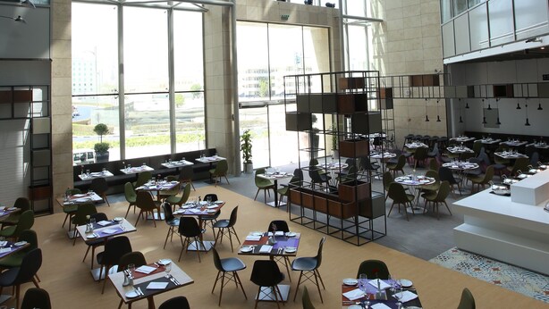 A spacious dining area with high ceilings and large windows, featuring multiple tables and chairs arranged for dining. - ibis Styles Dubai Jumeira (Dubai)